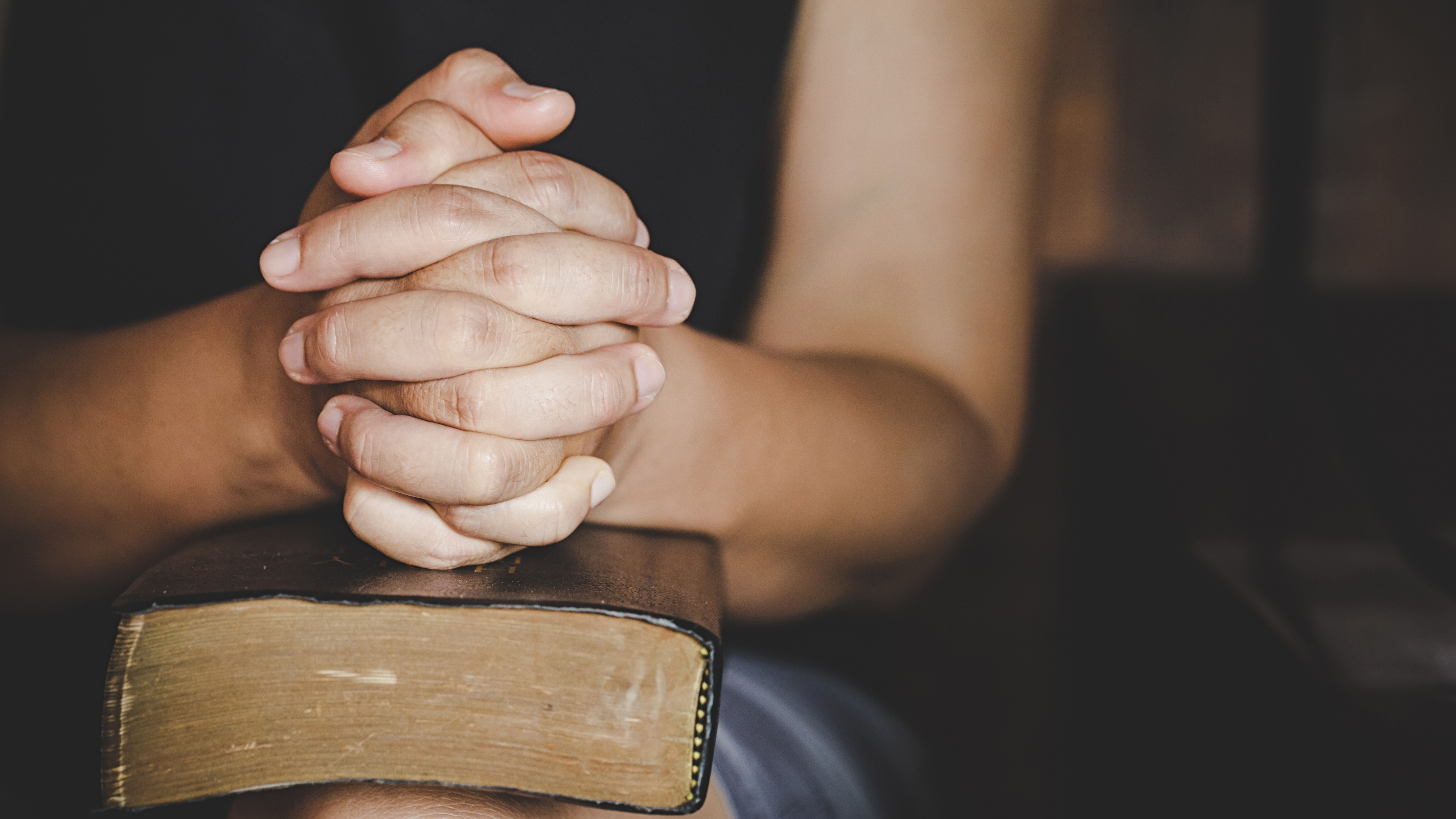 Folded praying hands resting on a Bible