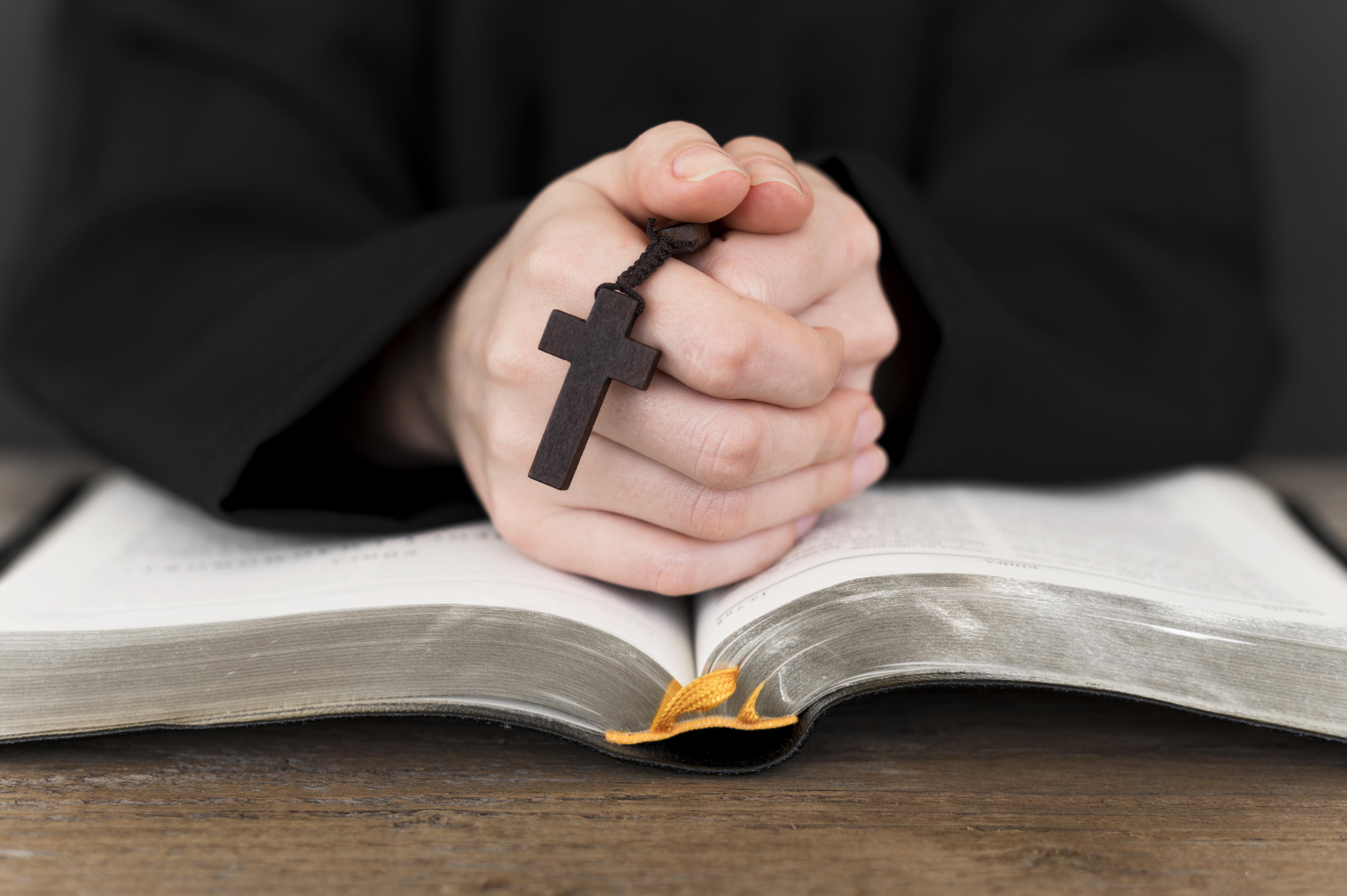 Person praying with cross and open Bible